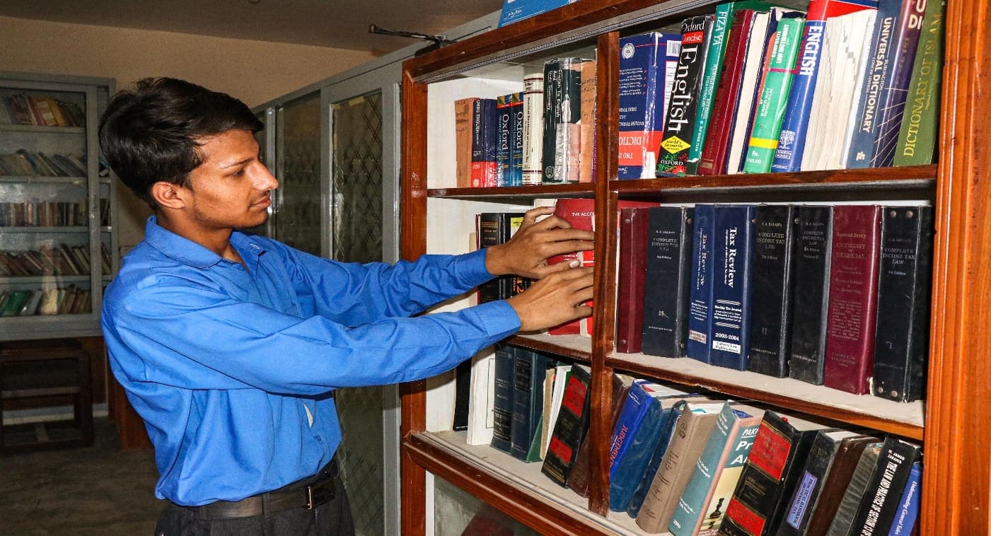 A student selecting a reference volume from the library shelves